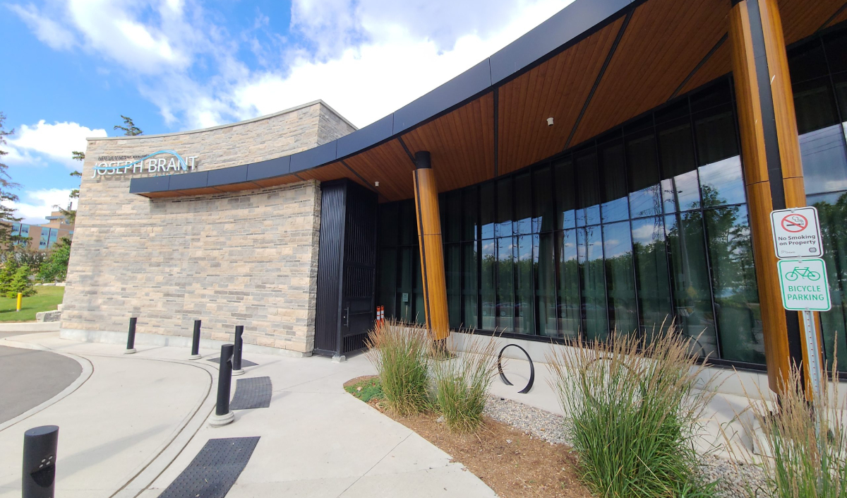 Modern stone and glass building with a curved entrance labeled "Joseph Brant Museum," featuring bicycle parking and a no smoking sign near the front.