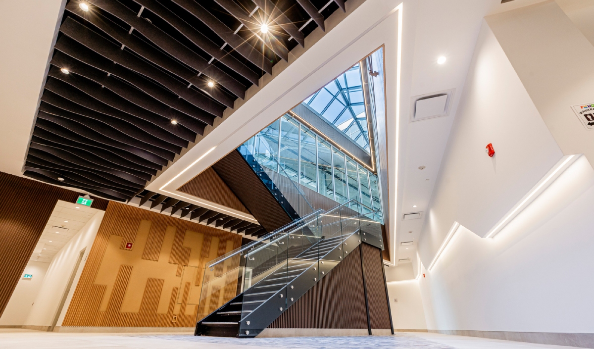 Modern indoor stairwell with glass railing, geometric ceiling panels, and a skylight allowing natural light into the space.
