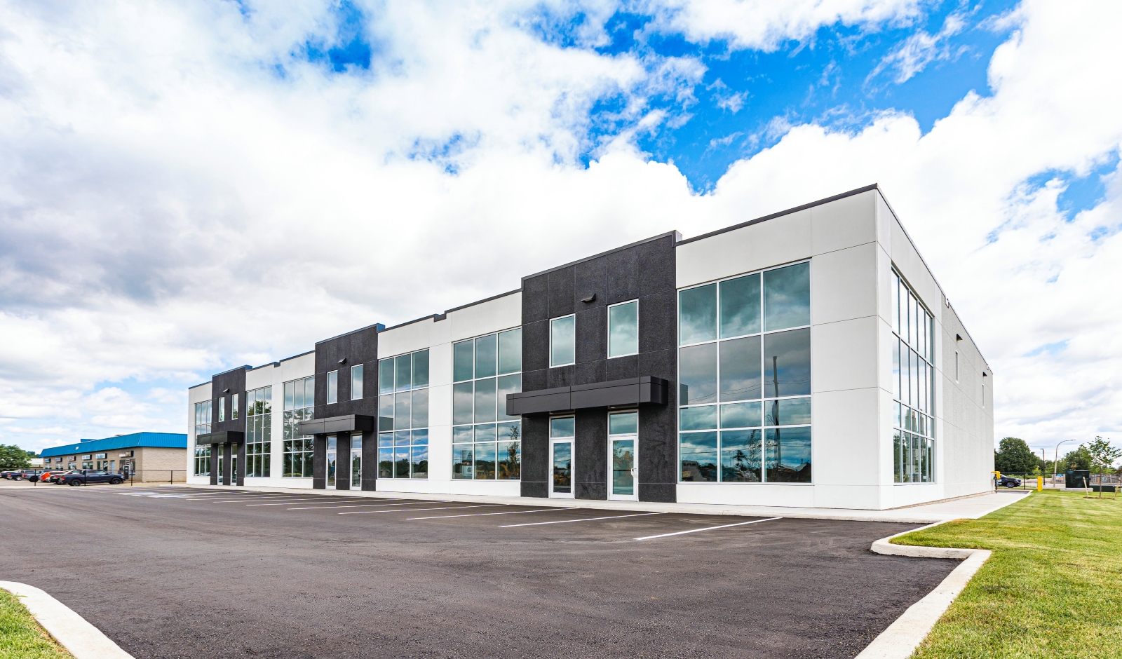 Modern, two-story commercial building with large glass windows and an empty parking lot, under a partly cloudy sky.