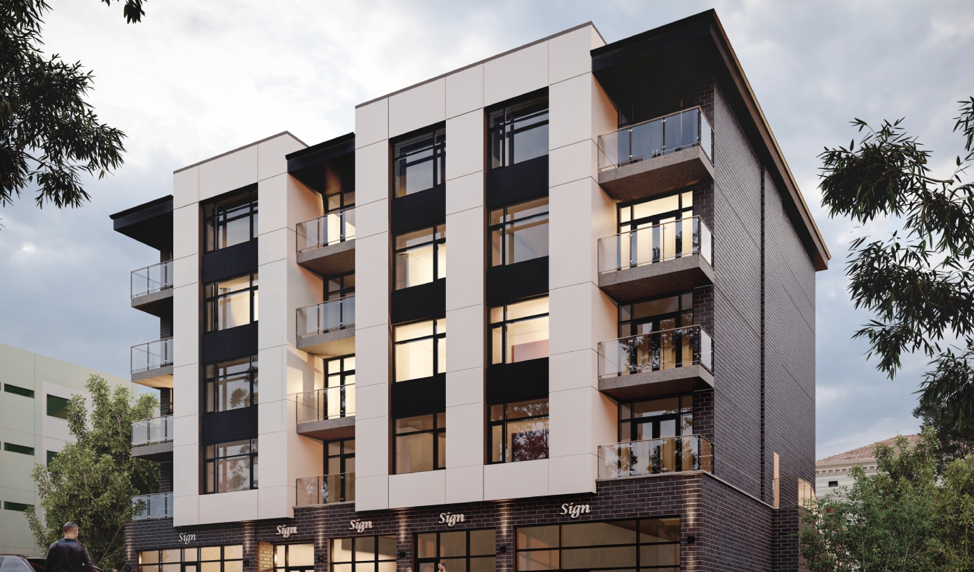 Modern four-story apartment building with balconies, large windows, and retail shops on the ground floor, surrounded by trees and lit by the evening sky.