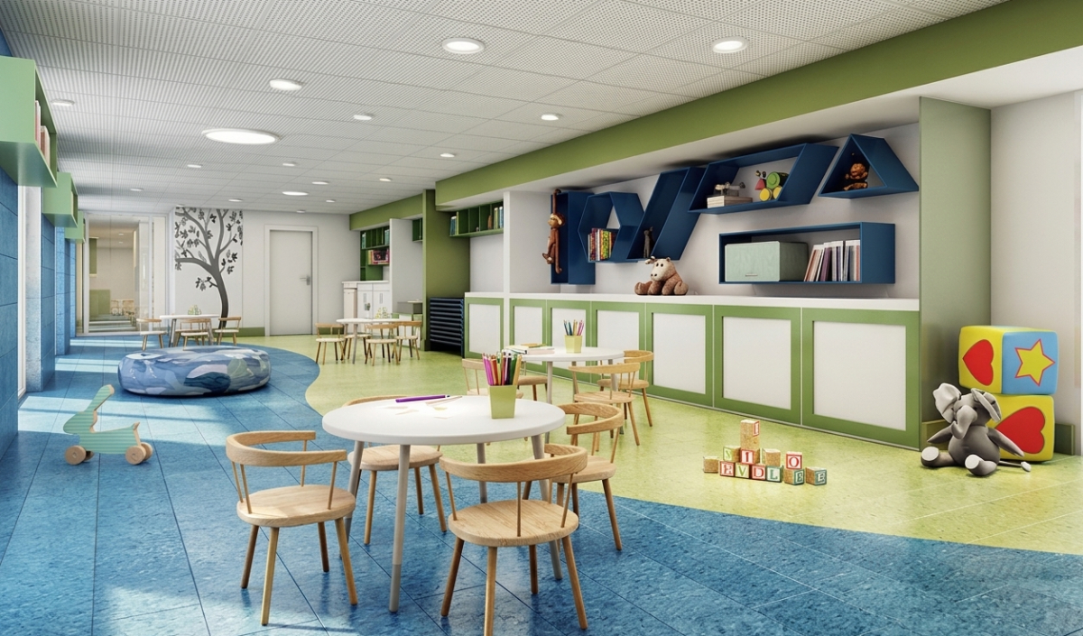 Bright, organized classroom with small tables, chairs, toys, bookshelves, and colorful decor. A mural tree is on the wall, and natural light fills the room.