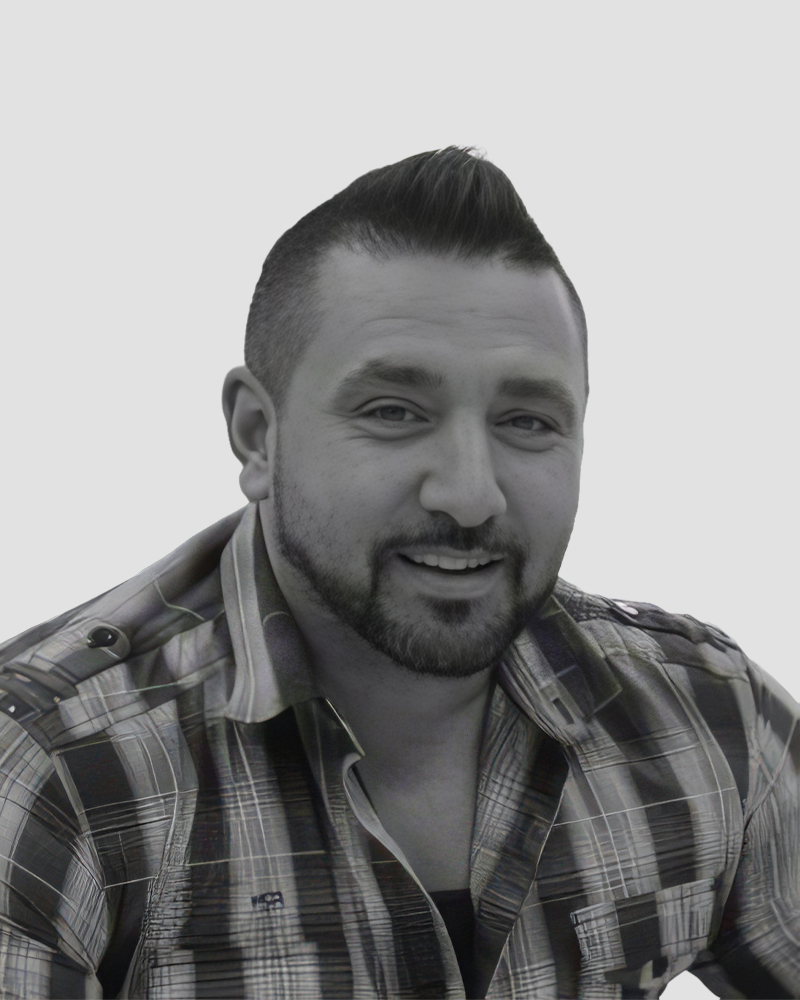 A man with a short, styled haircut and a beard, wearing a plaid button-down shirt.