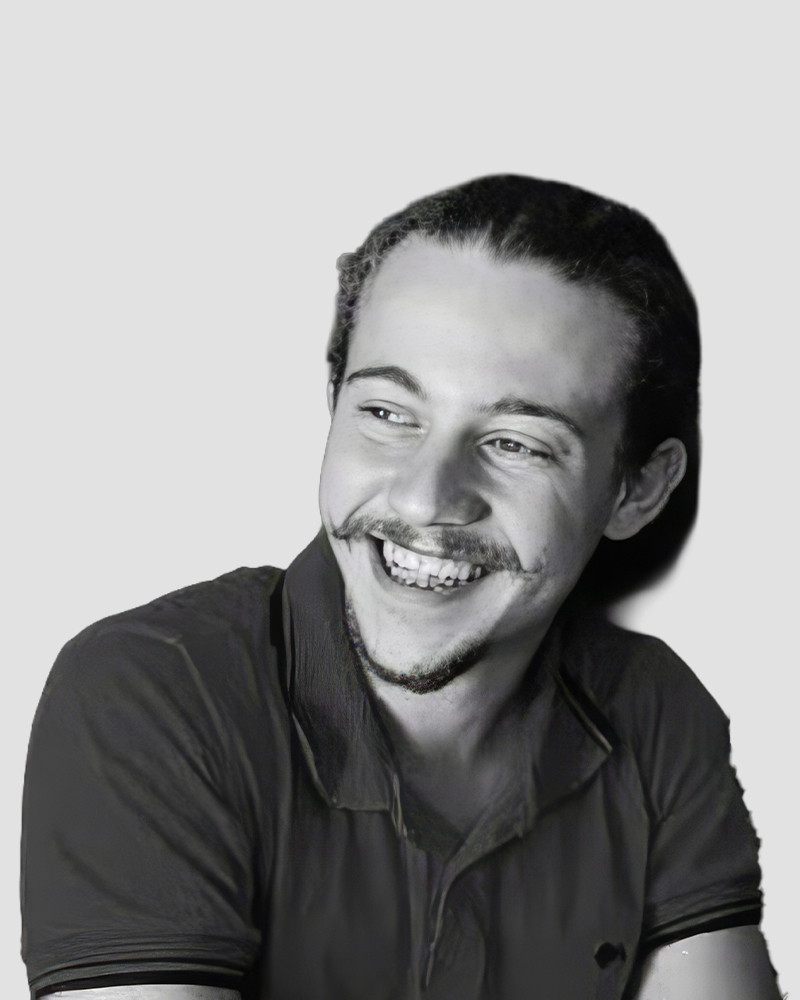 A young man with a mustache and goatee smiling and looking to the side.