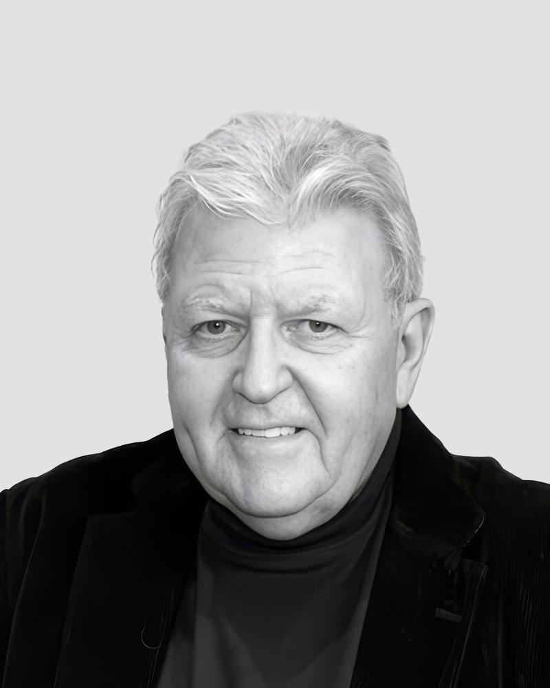 Headshot of an older man with white hair wearing a black turtleneck and jacket.