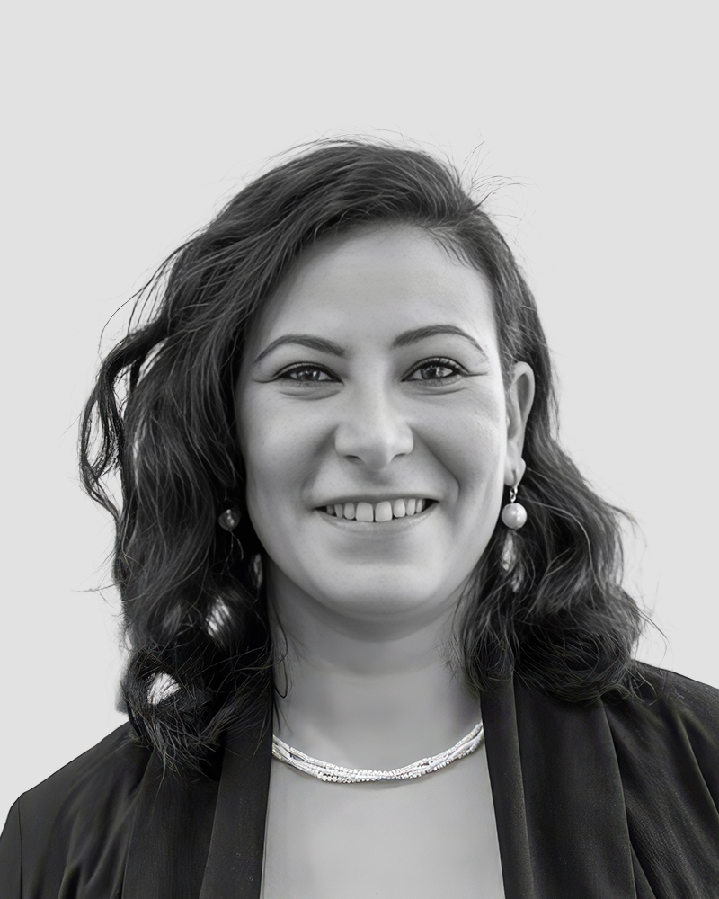 A portrait of a smiling woman wearing pearl earrings and a multi-strand necklace.